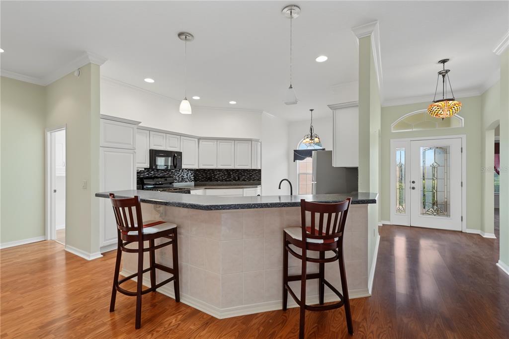 A kitchen with white cabinets, a dark countertop breakfast bar, and two wooden bar stools — 556 KINGSTON WAY, THE VILLAGES, FL