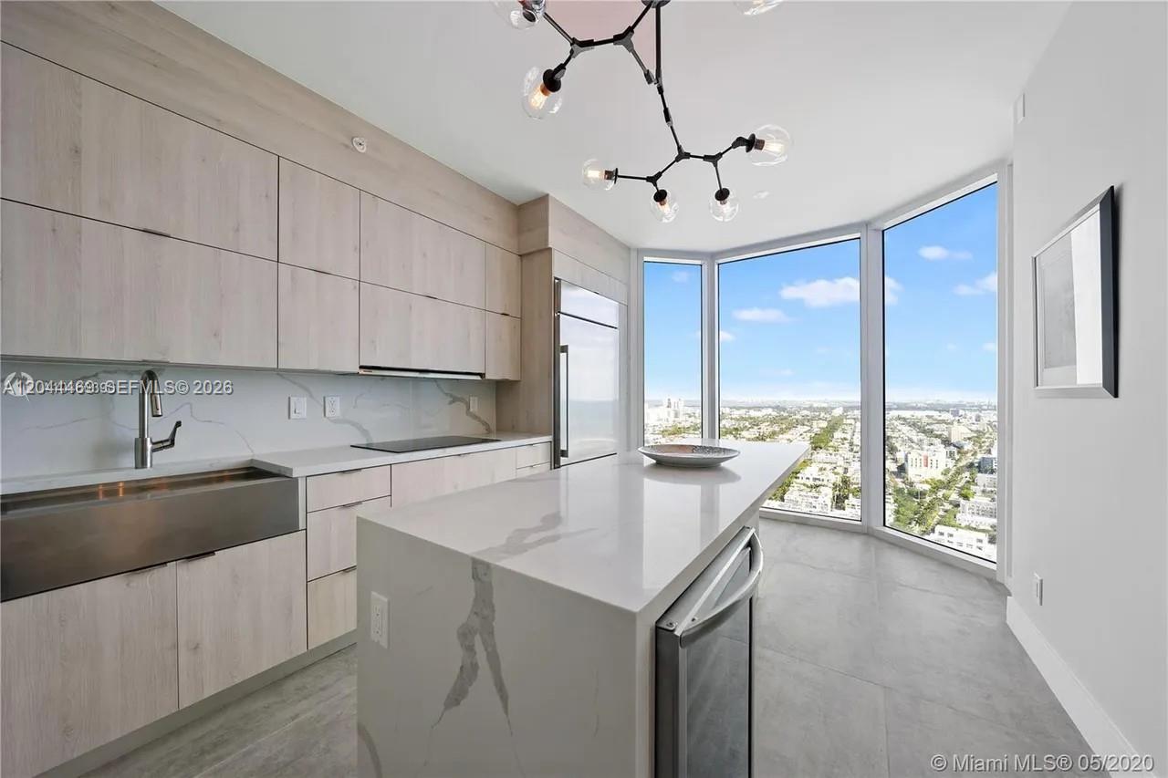 A modern kitchen features light wood cabinetry, a white marble island, and floor-to-ceiling windows — 300 S Pointe Dr # 3604, Miami Beach FL 33139, MIAMI BEACH, FL