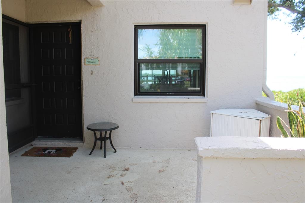 A concrete patio features a dark front door, a small round table, and a window — 1813 MARINER DRIVE UNIT 151, TARPON SPRINGS, FL