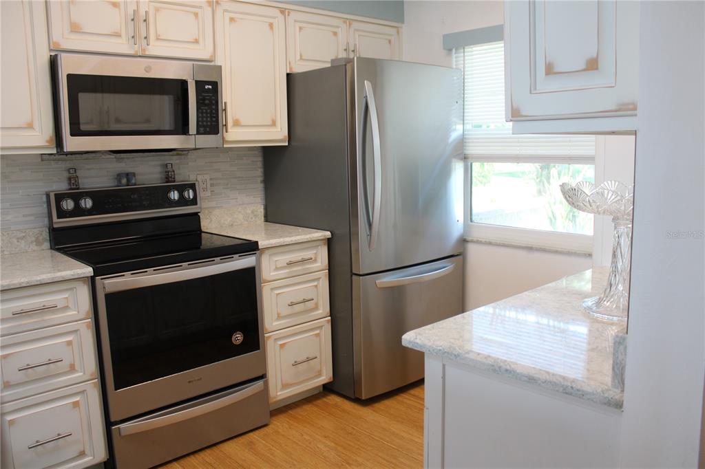A kitchen features stainless steel appliances, light-colored cabinets with distressed edges, and granite countertops — 1813 MARINER DRIVE UNIT 151, TARPON SPRINGS, FL