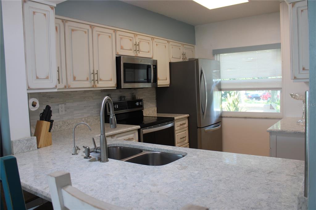 A kitchen with white distressed cabinets, stainless steel appliances, and light-colored granite countertops — 1813 MARINER DRIVE UNIT 151, TARPON SPRINGS, FL