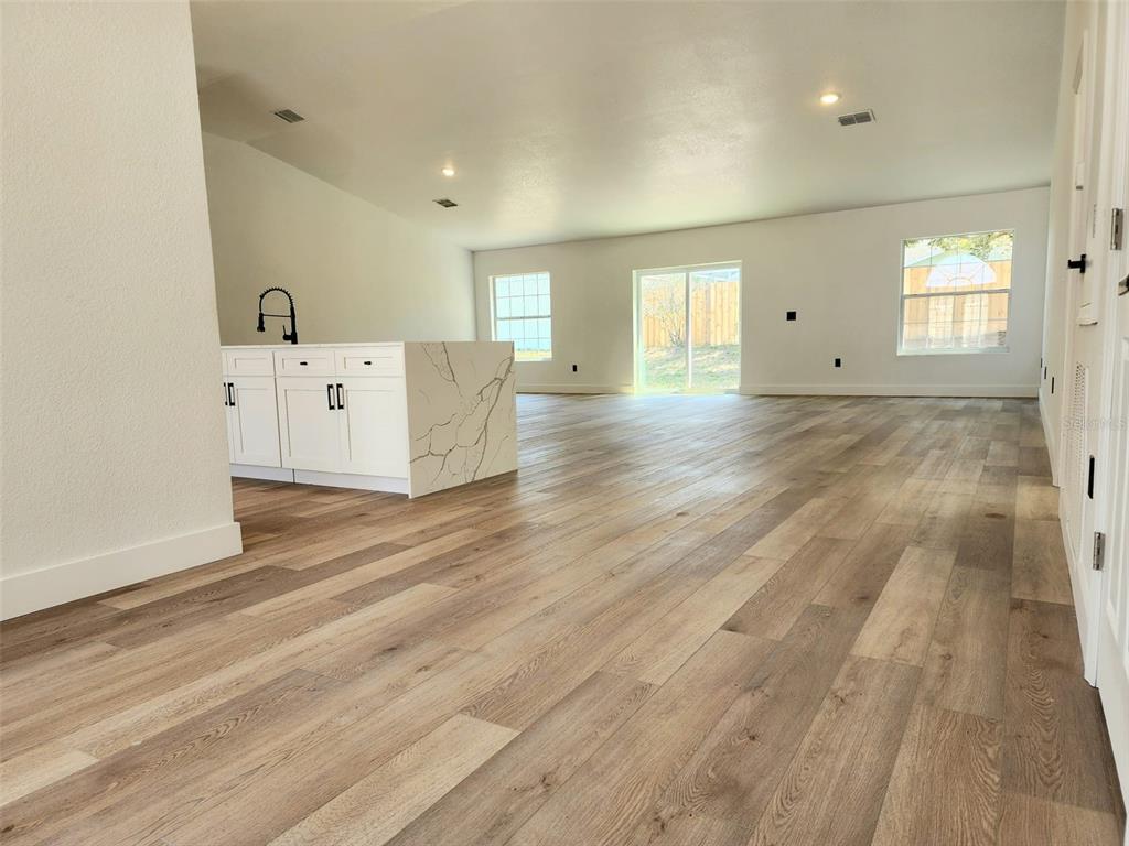 An open-concept living room and kitchen featuring white cabinetry, marble countertops, and wood-look flooring — 1032 CONCERT AVENUE, SPRING HILL, FL