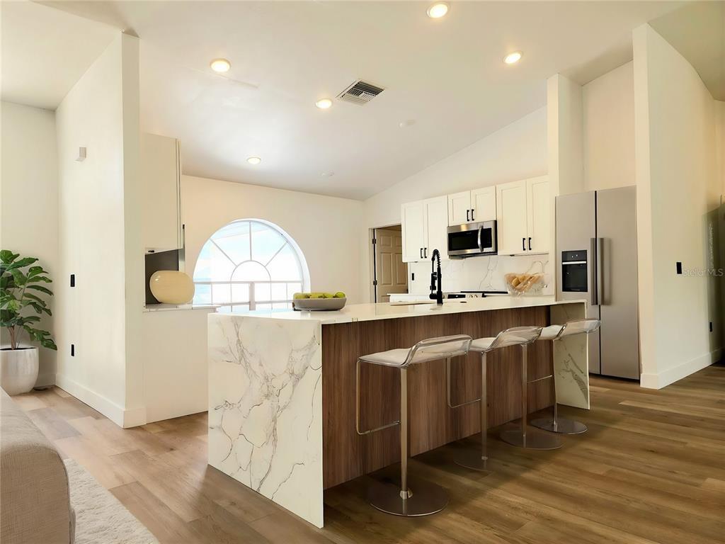 A kitchen island with a marble countertop sits in an open-concept room with wood flooring — 1032 CONCERT AVENUE, SPRING HILL, FL