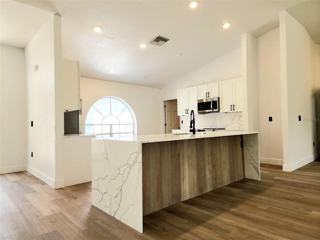 A kitchen features a waterfall island with bar stools, white cabinets, and a large arched window — 1032 CONCERT AVENUE, SPRING HILL, FL