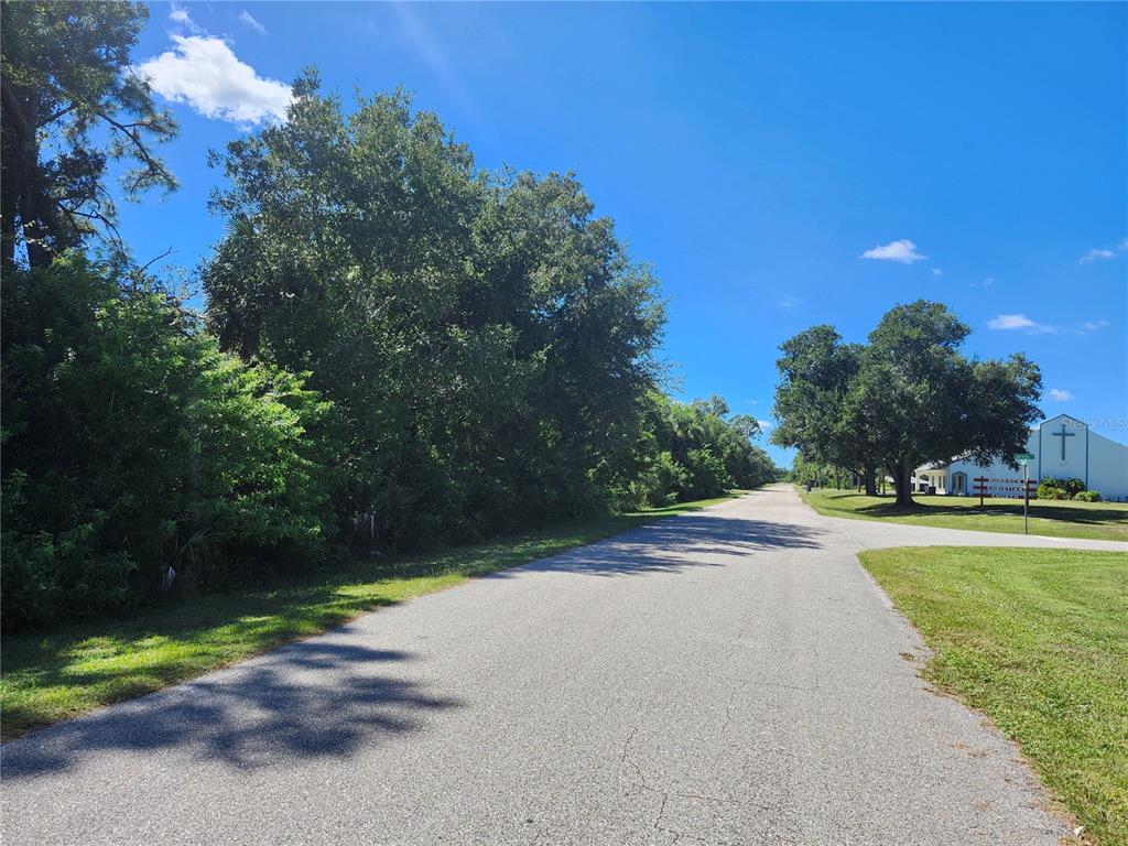 A paved road runs past a wooded lot toward a building with a cross — 17517 ELMWOOD AVENUE, PORT CHARLOTTE, FL