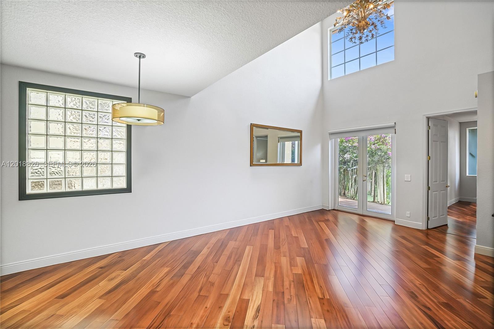 An empty room with high ceilings, hardwood floors, a glass block window, and French doors — 1282 Grant Ct, Hollywood FL 33019, HOLLYWOOD, FL