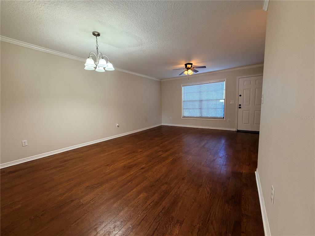 An empty living room features dark wood-look flooring, a ceiling fan, and a chandelier — 3220 OAK LAWN PLACE PLACE UNIT 210, WINTER PARK, FL