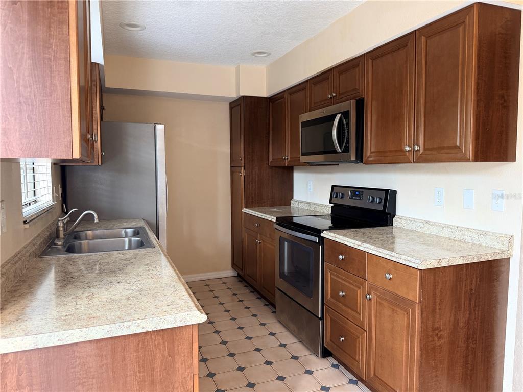 A kitchen features wood cabinets, stainless steel appliances, and light-colored laminate countertops — 3220 OAK LAWN PLACE PLACE UNIT 210, WINTER PARK, FL