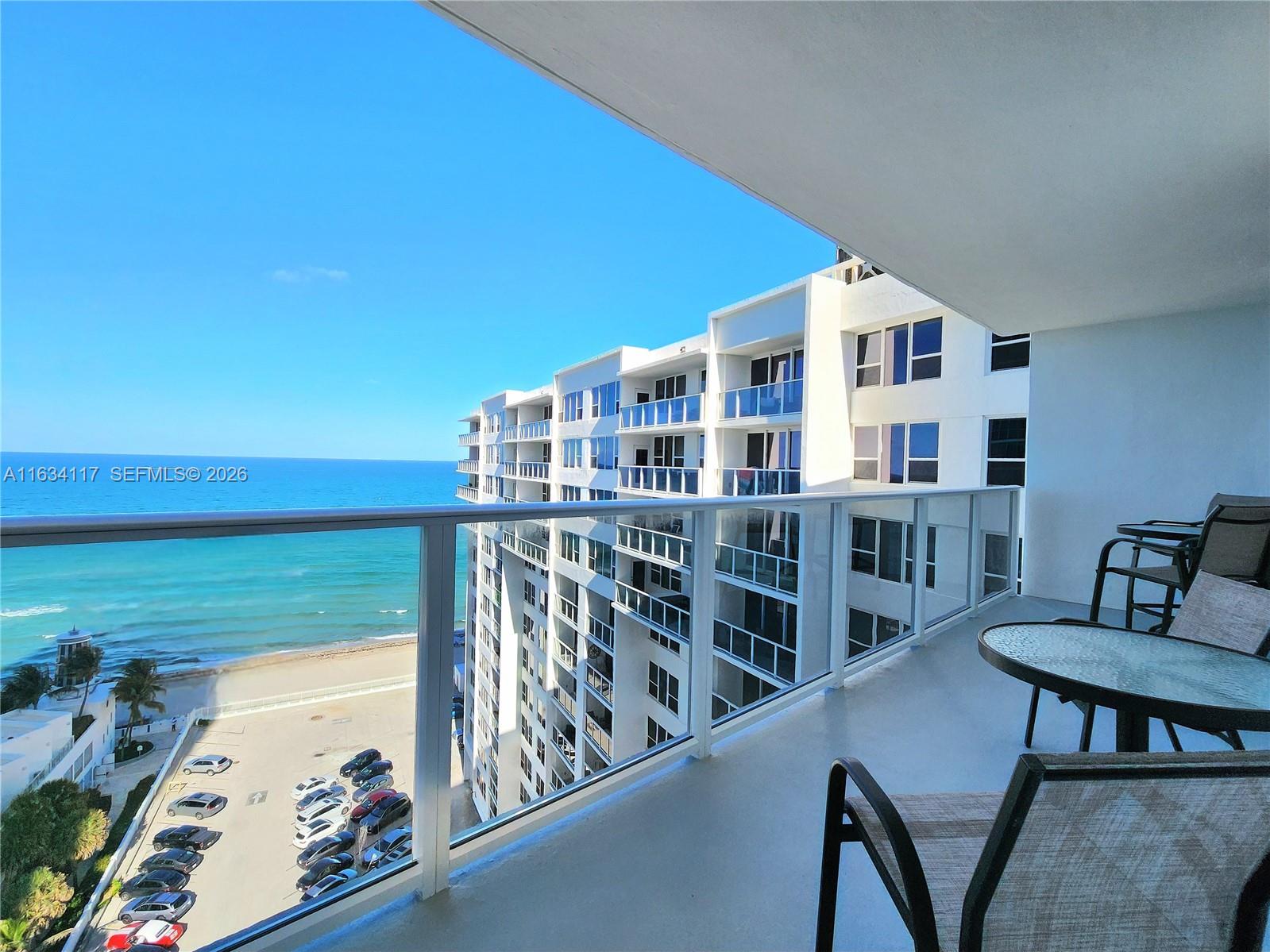 A balcony with outdoor furniture overlooks a parking lot, beach, and the ocean — 3505 S Ocean Dr # 1406, Hollywood FL 33019, HOLLYWOOD, FL