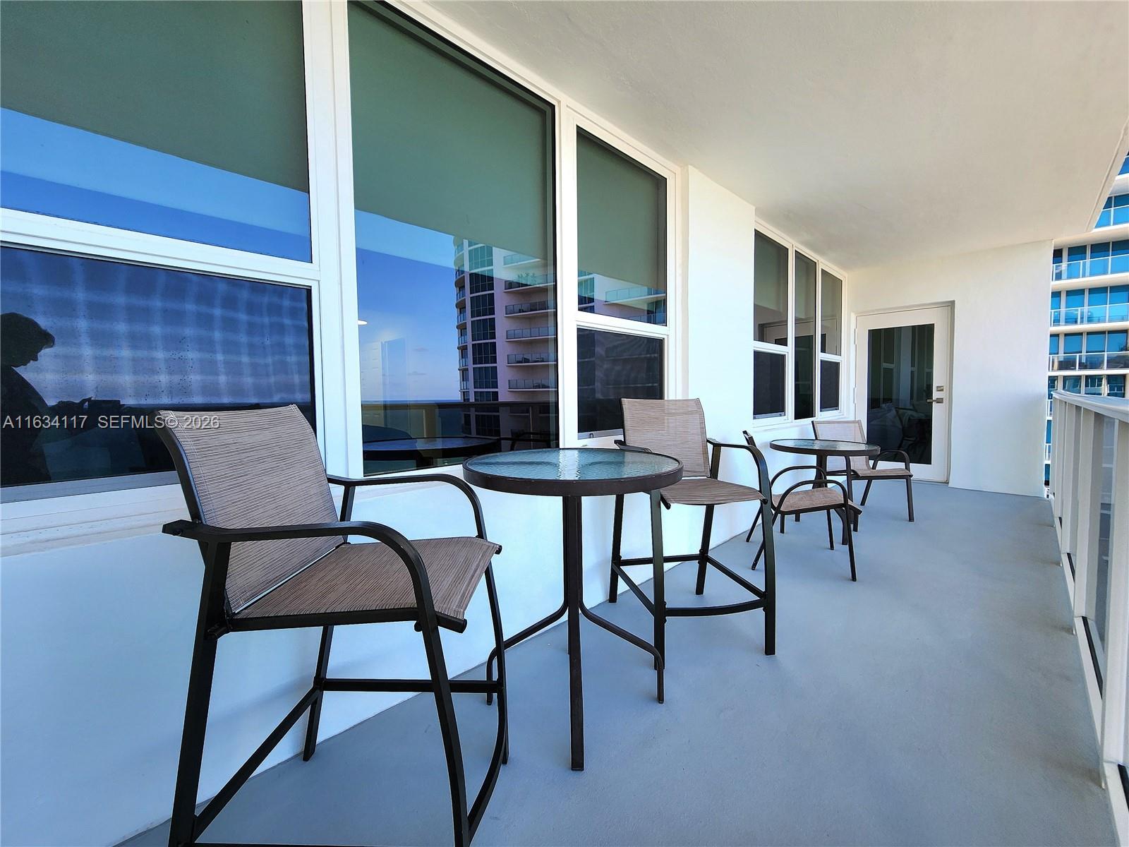 A balcony features two small round tables and four chairs set against a white building — 3505 S Ocean Dr # 1406, Hollywood FL 33019, HOLLYWOOD, FL