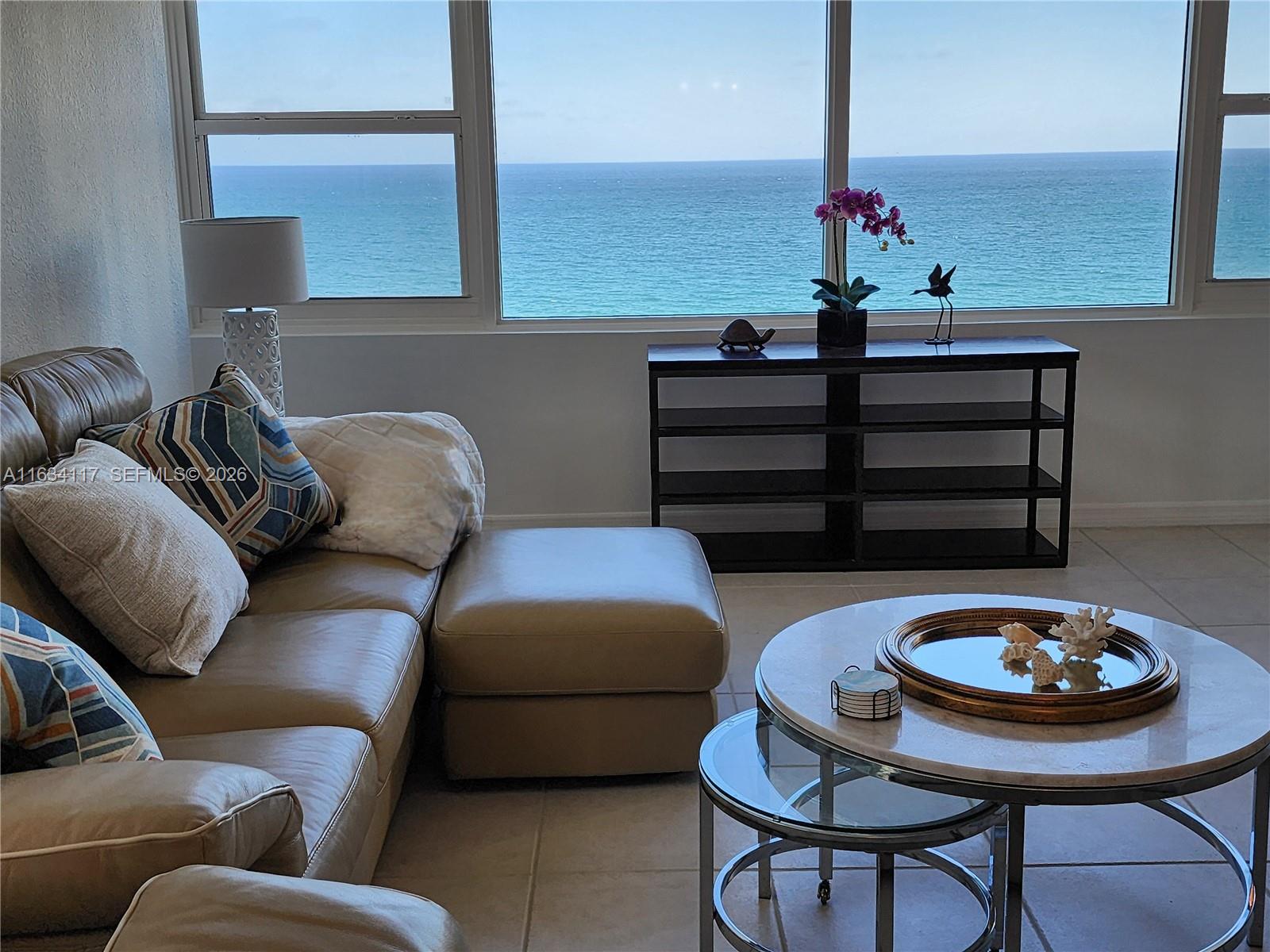 A living room with a leather sofa and coffee table overlooks the ocean through windows — 3505 S Ocean Dr # 1406, Hollywood FL 33019, HOLLYWOOD, FL