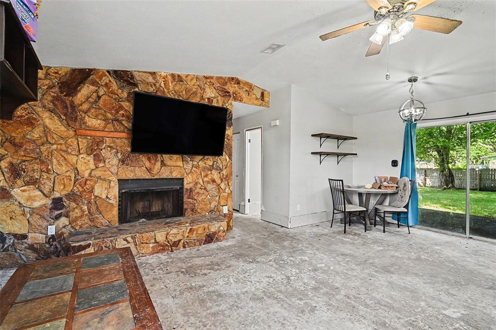 A living room features a stone fireplace, a ceiling fan, and an unfinished concrete floor — 1980 OLD DIXIE HIGHWAY, TITUSVILLE, FL