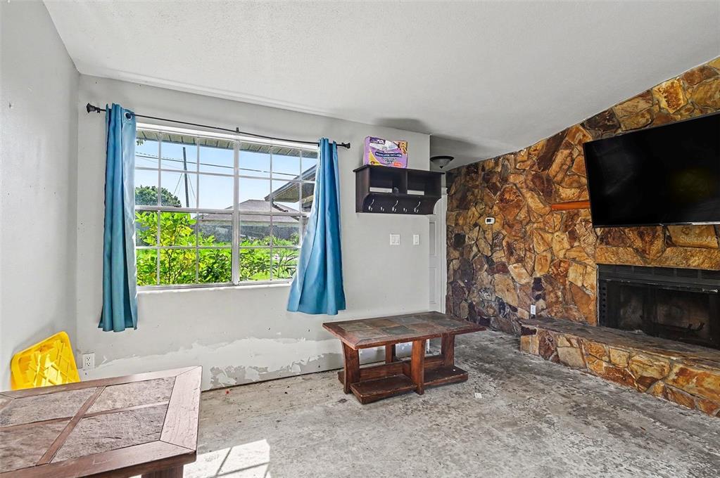 A living room features a stone fireplace, a large window with blue curtains, and concrete floors — 1980 OLD DIXIE HIGHWAY, TITUSVILLE, FL