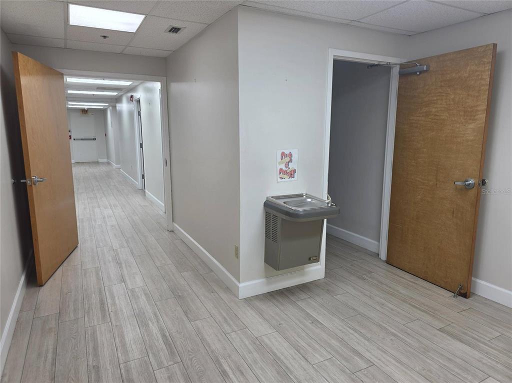 A hallway with wood-look tile flooring features a water fountain and two open wooden doors — 2525 HARBOR BOULEVARD UNIT 101, PORT CHARLOTTE, FL