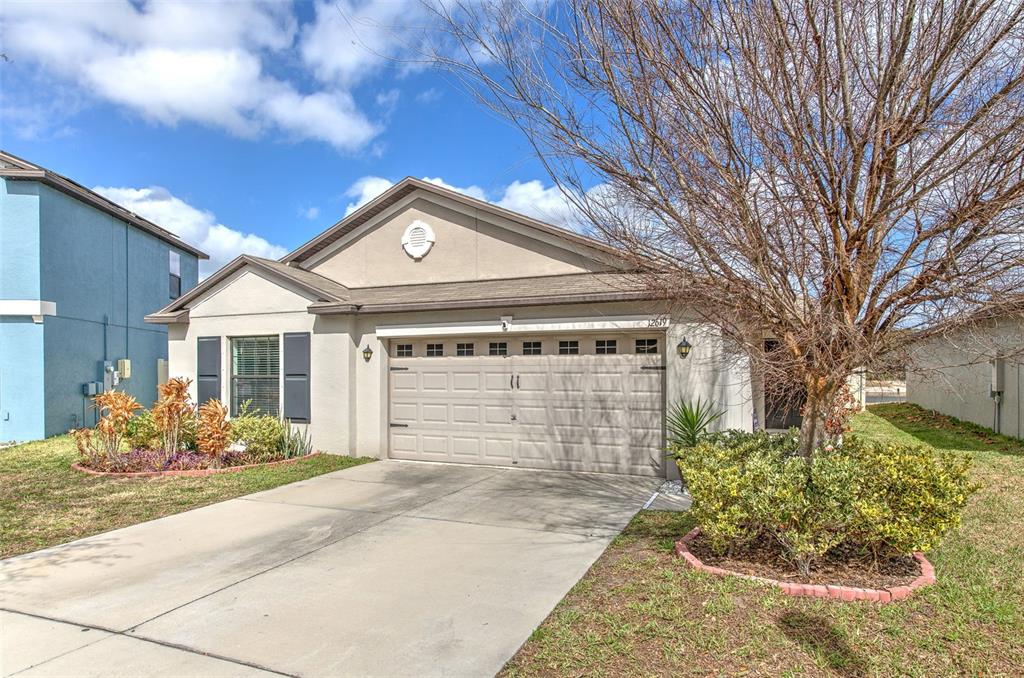 A single-story house with a beige stucco exterior, a two-car garage, and a concrete driveway — 12619 LEMON PEPPER DRIVE, RIVERVIEW, FL
