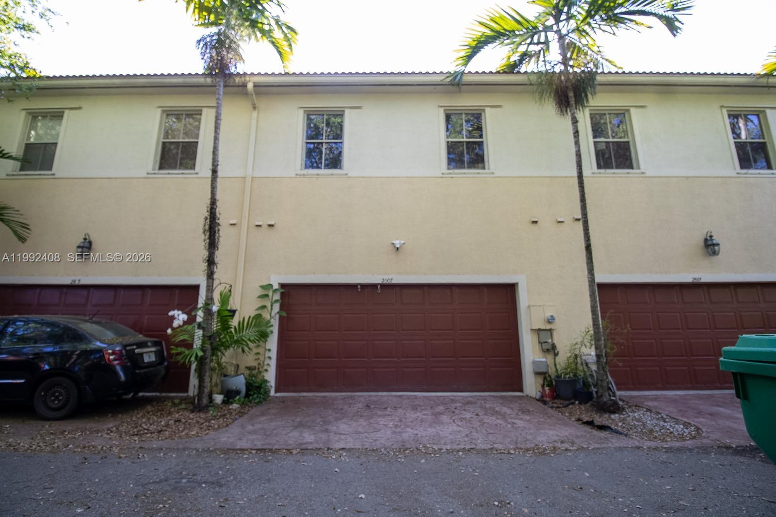 A row of townhouses features beige stucco walls, red garage doors, and tall palm trees — 2607 SW 99th Way, Miramar FL 33025, MIRAMAR, FL