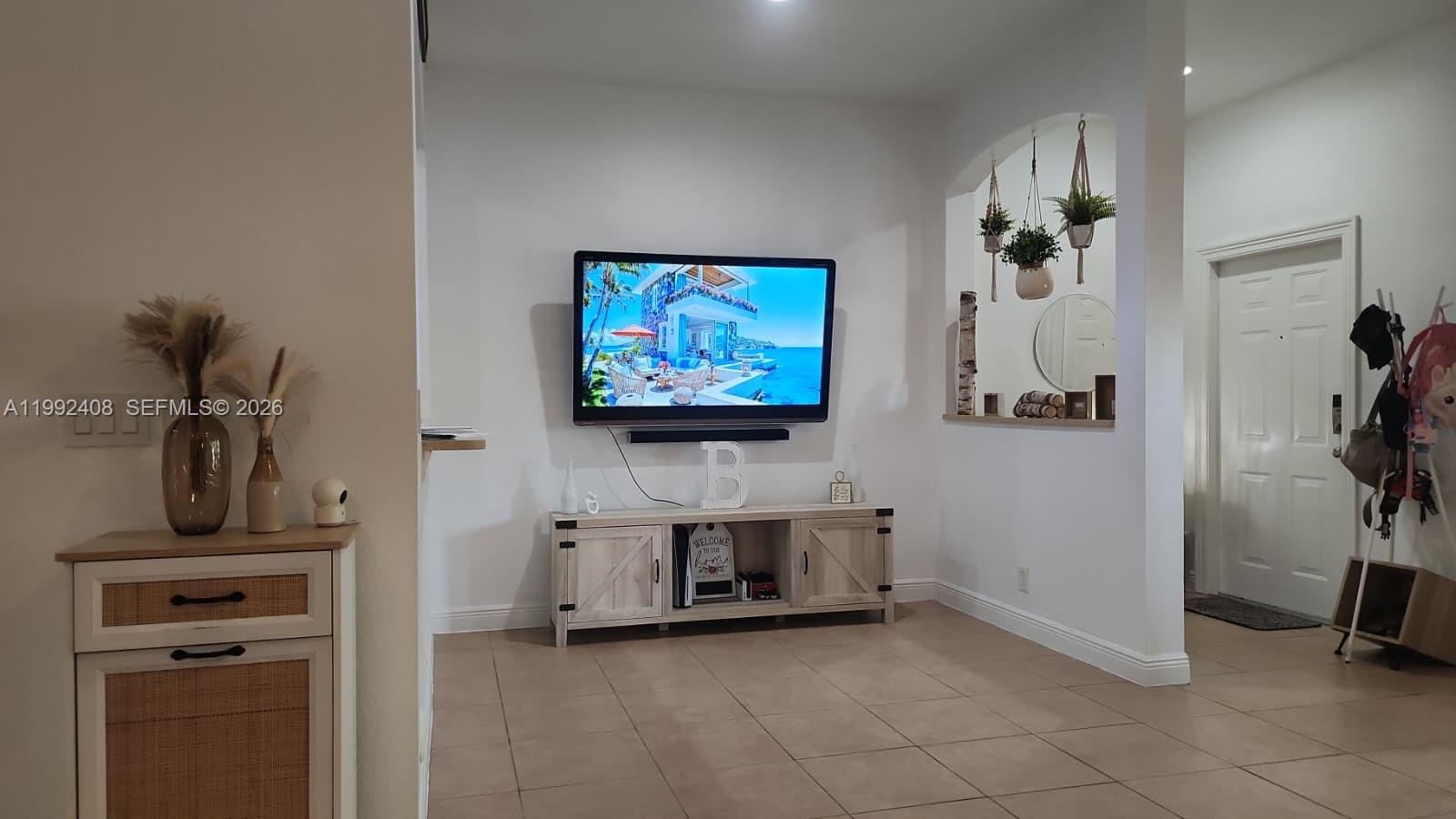 A living room features a wall-mounted television, a light wood media console, and an arched alcove — 2607 SW 99th Way, Miramar FL 33025, MIRAMAR, FL