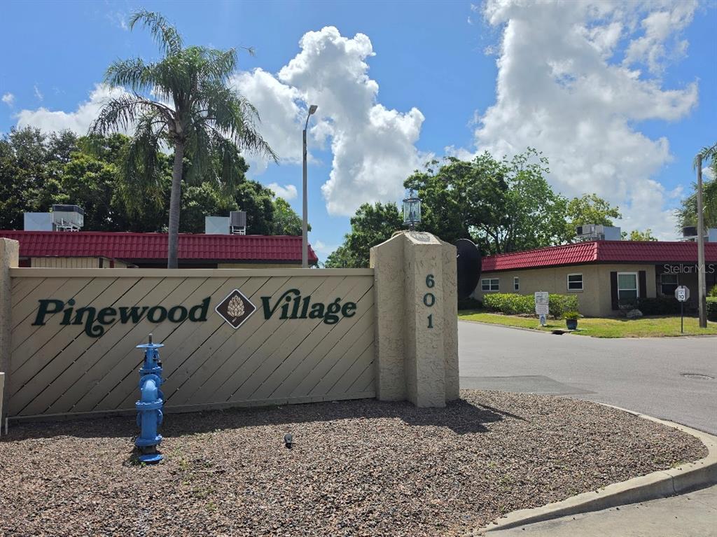 A beige sign for Pinewood Village stands near a blue fire hydrant and a road — 601 N HERCULES AVENUE UNIT 1205, CLEARWATER, FL