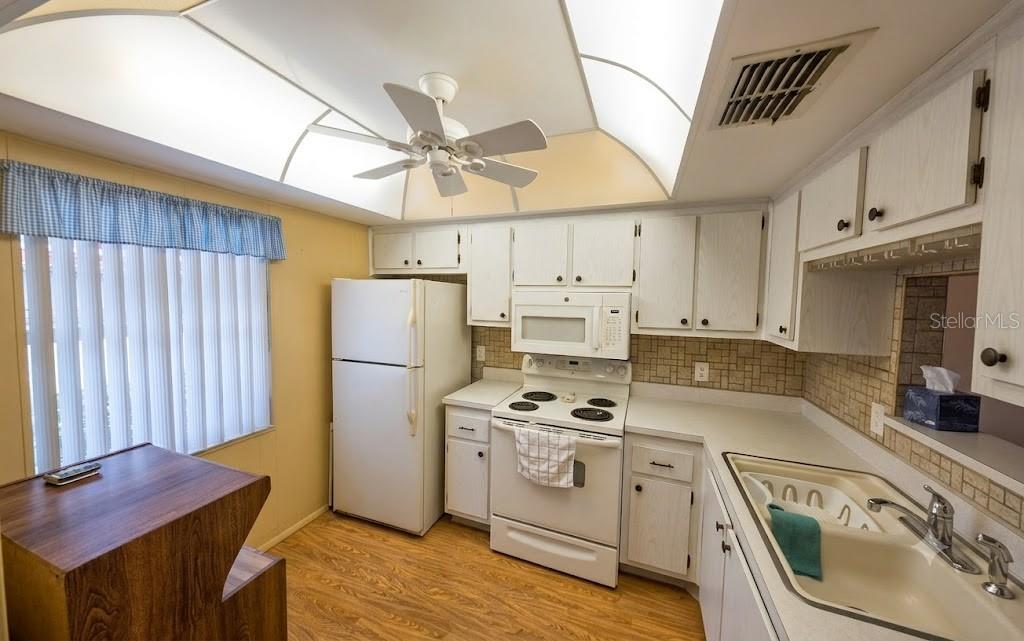 A kitchen with white cabinets, white appliances, a tiled backsplash, and a vaulted ceiling — 601 N HERCULES AVENUE UNIT 1205, CLEARWATER, FL