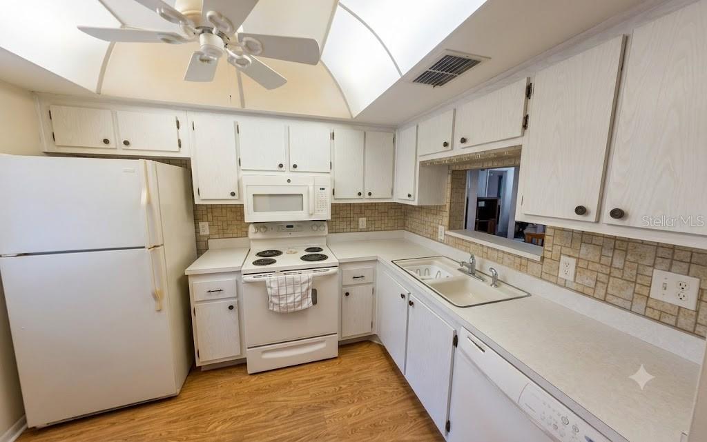 A kitchen with white cabinets, white appliances, a tiled backsplash, and a ceiling fan — 601 N HERCULES AVENUE UNIT 1205, CLEARWATER, FL