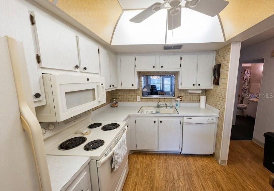 A kitchen with white cabinets, white appliances, a pass-through window, and wood-look flooring — 601 N HERCULES AVENUE UNIT 1205, CLEARWATER, FL