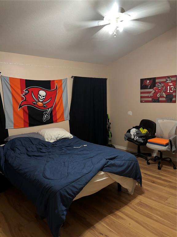 A bedroom features wood-look flooring, a Tampa Bay Buccaneers flag, and a wall-mounted sports print — 27450 SUGAR LOAF DRIVE, WESLEY CHAPEL, FL
