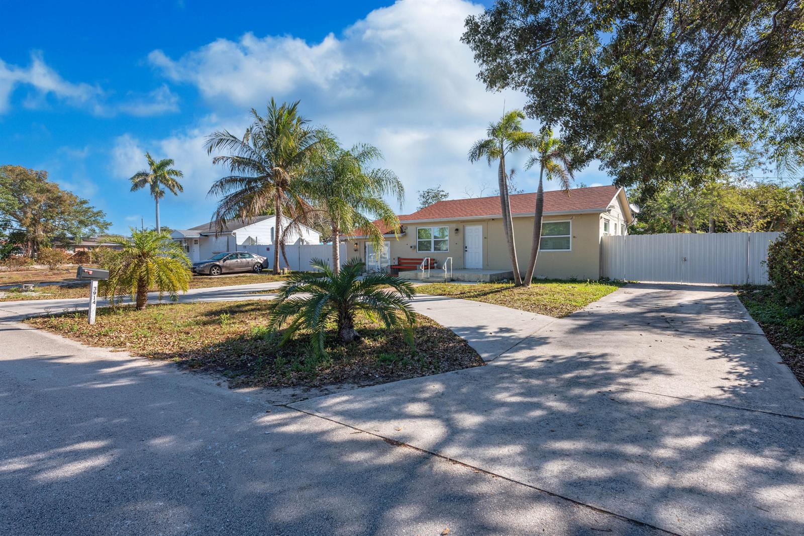 A single-story house with a concrete driveway, palm trees, and a white fence — 3914 Serubi Avenue, Palm Springs FL 33461, PALM SPRINGS, FL