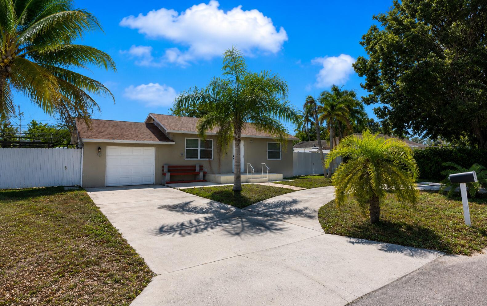 A single-story house with a white garage door, a red bench, and several palm trees — 3914 Serubi Avenue, Palm Springs FL 33461, PALM SPRINGS, FL