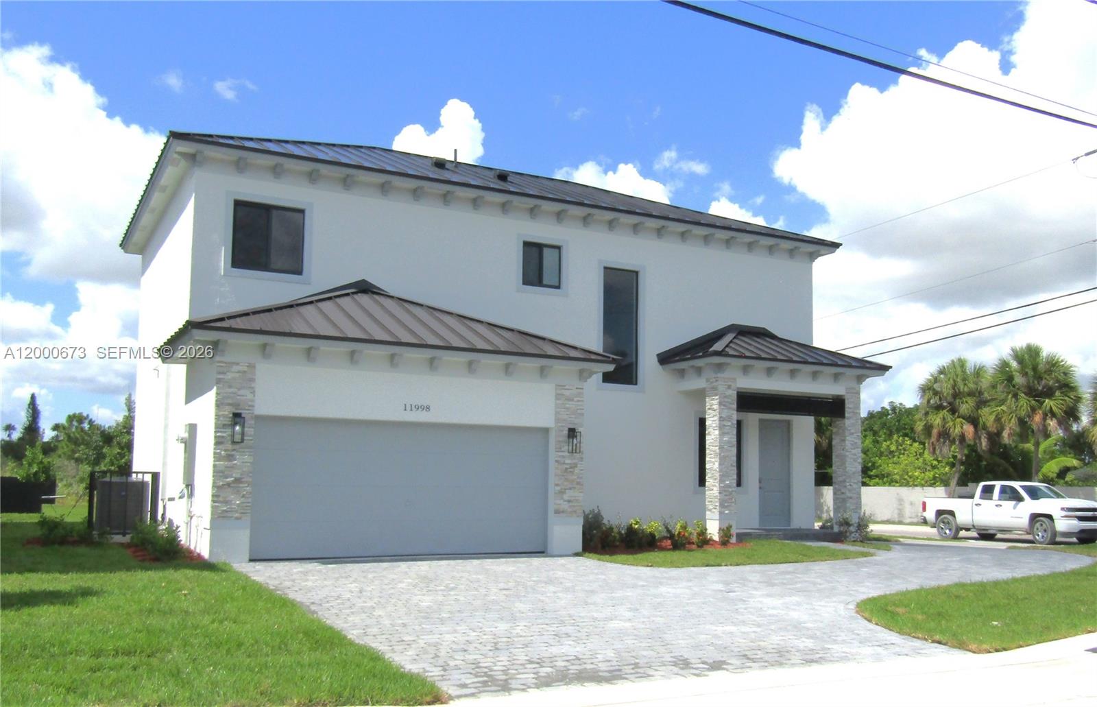 A two-story house with a metal roof, white stucco walls, and a stone-accented garage — 11998 SW 232nd St, Miami FL 33170, MIAMI, FL