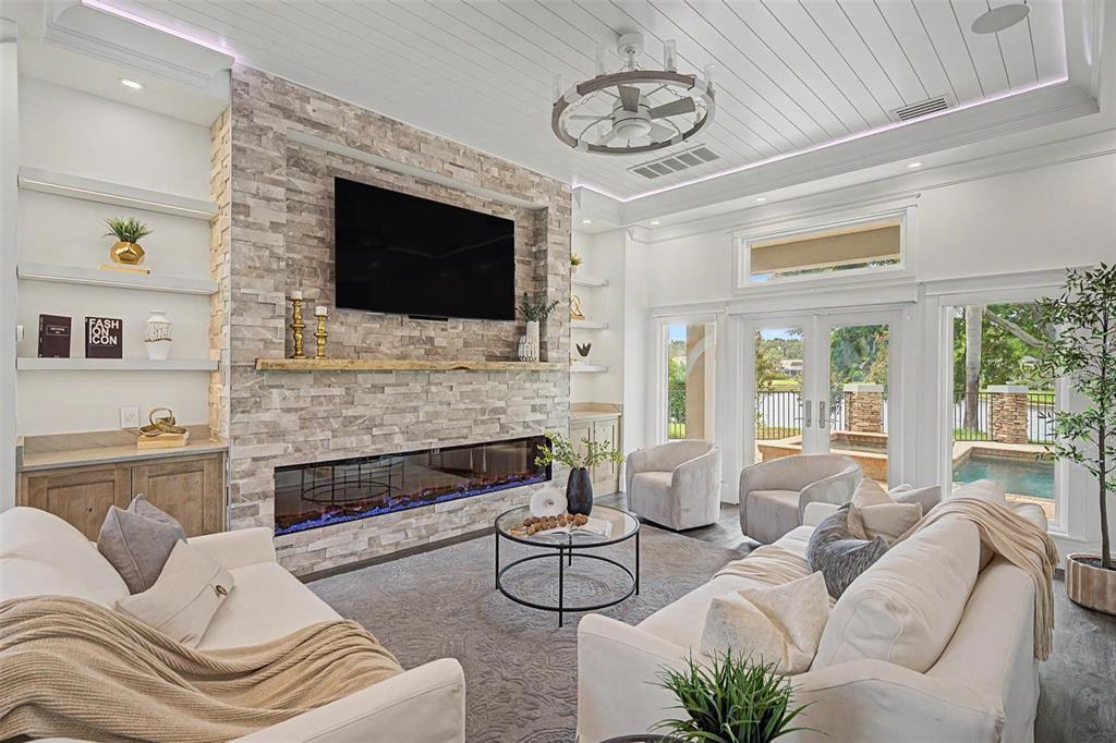 A living room features a stone fireplace, a wall-mounted television, and views of a pool — 3781 EXECUTIVE DRIVE, PALM HARBOR, FL