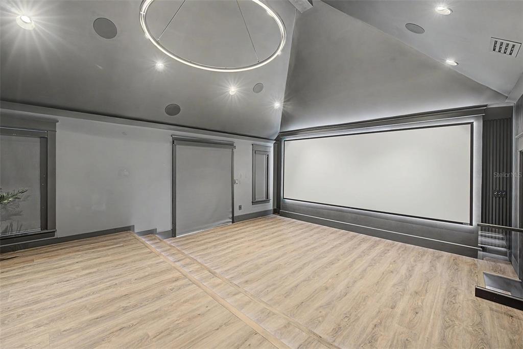 A home theater room features a large projection screen, vaulted ceilings, and light wood flooring — 3781 EXECUTIVE DRIVE, PALM HARBOR, FL