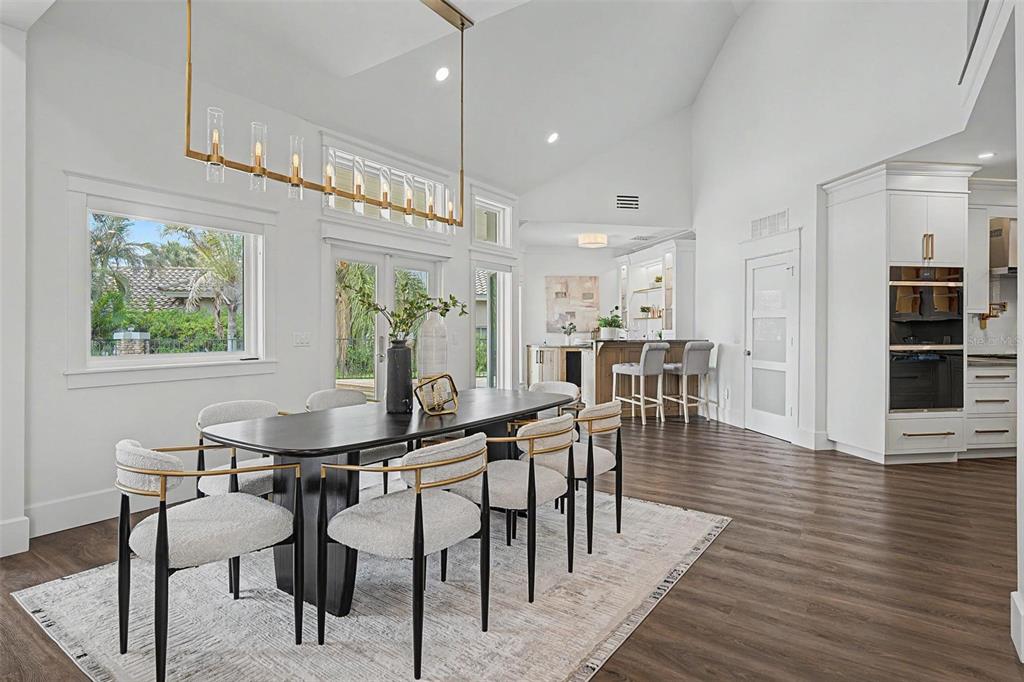 A dining area with a long black table, modern chairs, and a gold linear chandelier — 3781 EXECUTIVE DRIVE, PALM HARBOR, FL