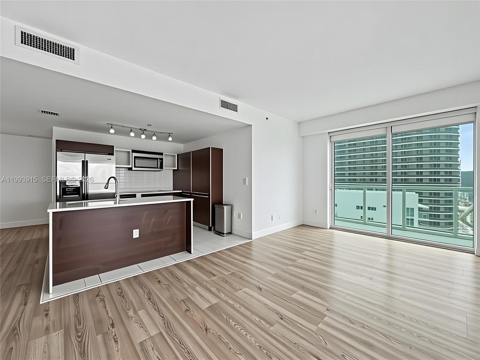 A modern kitchen with dark wood cabinetry and an island opens to a living area — 1900 N Bayshore Dr # 3811, Miami FL 33132, MIAMI, FL