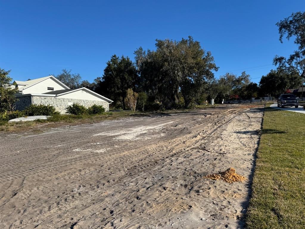 A dirt road leads past a white house with a stone facade toward mature trees — 1232 CR 17 ROAD N, LAKE PLACID, FL