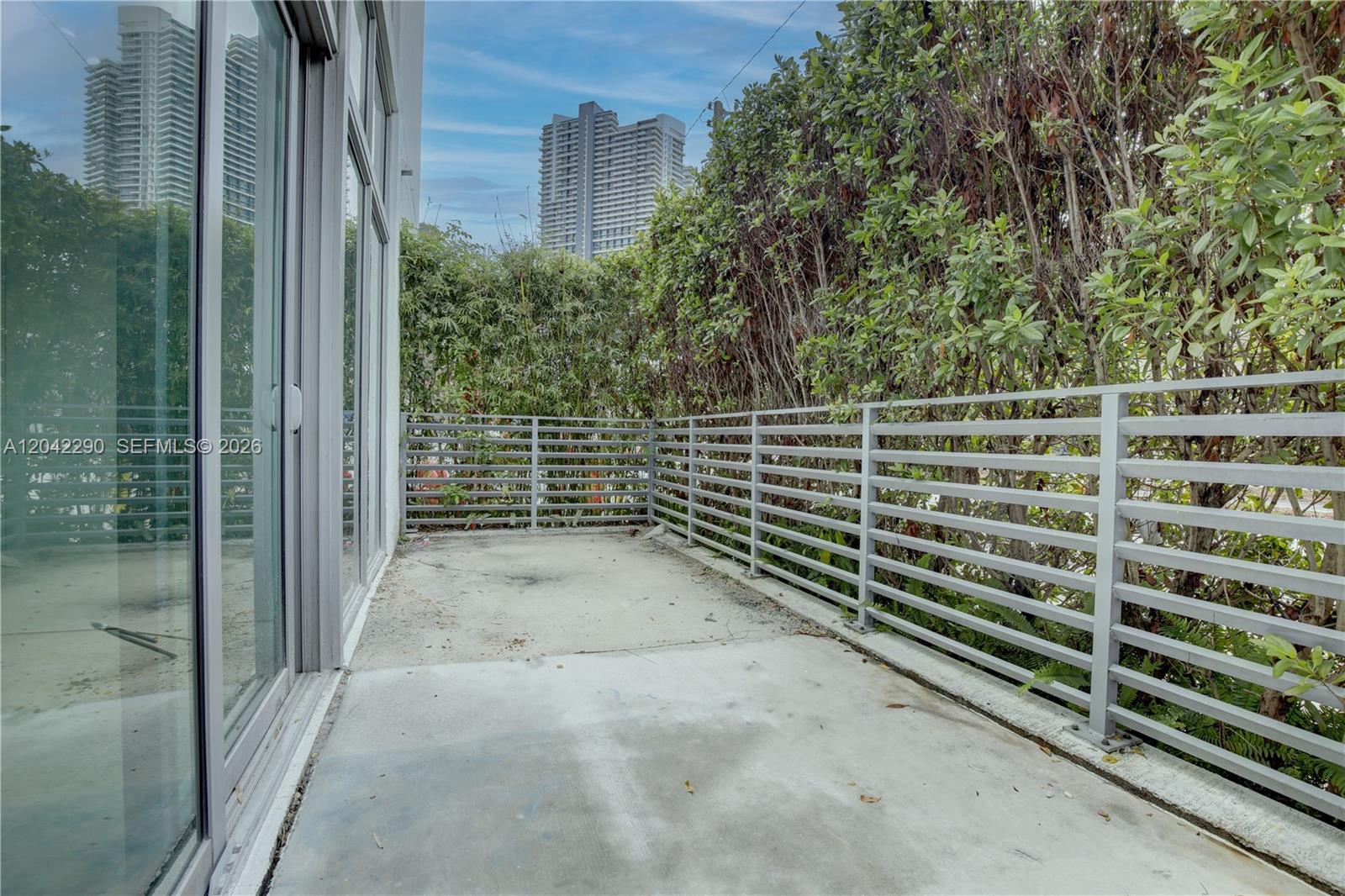 A concrete balcony features a gray metal railing and is enclosed by tall, dense hedges — 1600 SW 1st Ave # 09, Miami FL 33129, MIAMI, FL
