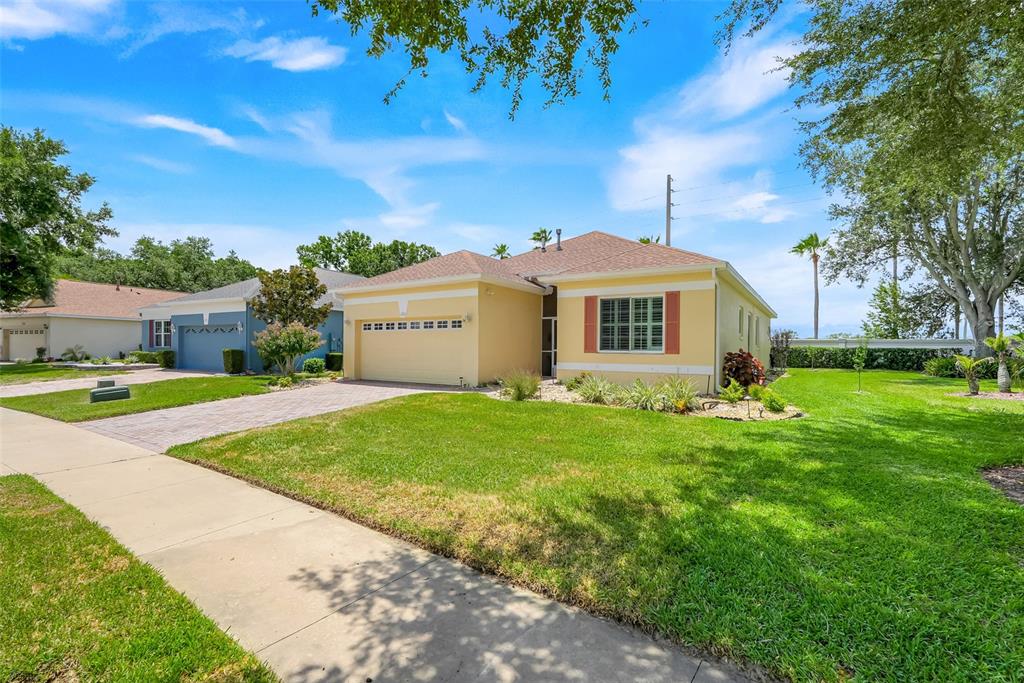 A yellow single-story house with a two-car garage and a green lawn under blue skies — 3003 PINNACLE COURT, CLERMONT, FL
