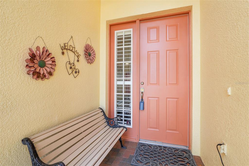 A peach-colored front door with a side window, a bench, and wall decor on a porch — 3003 PINNACLE COURT, CLERMONT, FL