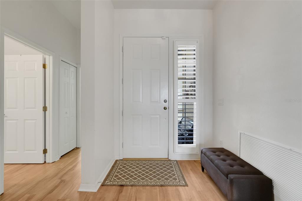 An entryway with light wood flooring, a white front door, a side window, and a bench — 3003 PINNACLE COURT, CLERMONT, FL