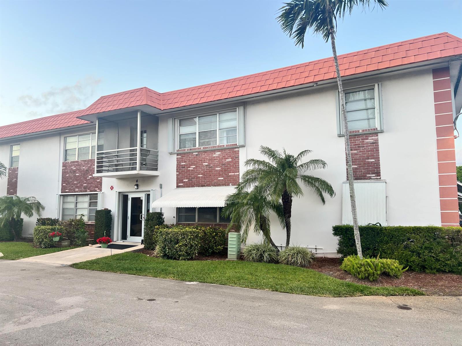 A two-story apartment building features a red tiled roof, brick accents, and a palm tree — 3550 NW 8th Avenue # 404, Pompano Beach FL 33064, POMPANO BEACH, FL