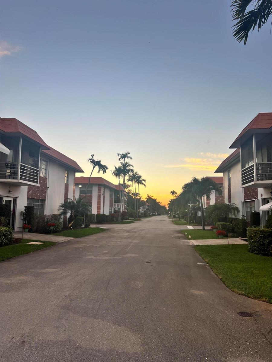 An exterior view of a residential street lined with two-story apartment buildings at sunset — 3550 NW 8th Avenue # 404, Pompano Beach FL 33064, POMPANO BEACH, FL