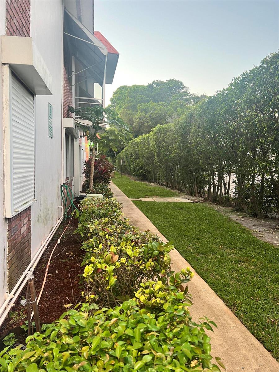 A view of a building exterior with a walkway, manicured hedges, and a grassy lawn — 3550 NW 8th Avenue # 404, Pompano Beach FL 33064, POMPANO BEACH, FL