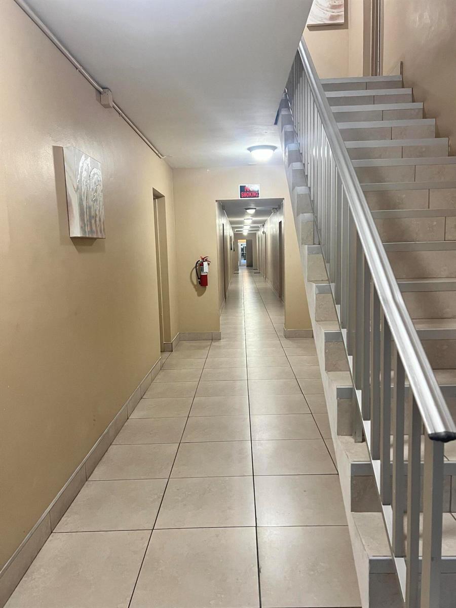 A tiled hallway features a staircase with a metal railing and a wall-mounted fire extinguisher — 3550 NW 8th Avenue # 404, Pompano Beach FL 33064, POMPANO BEACH, FL