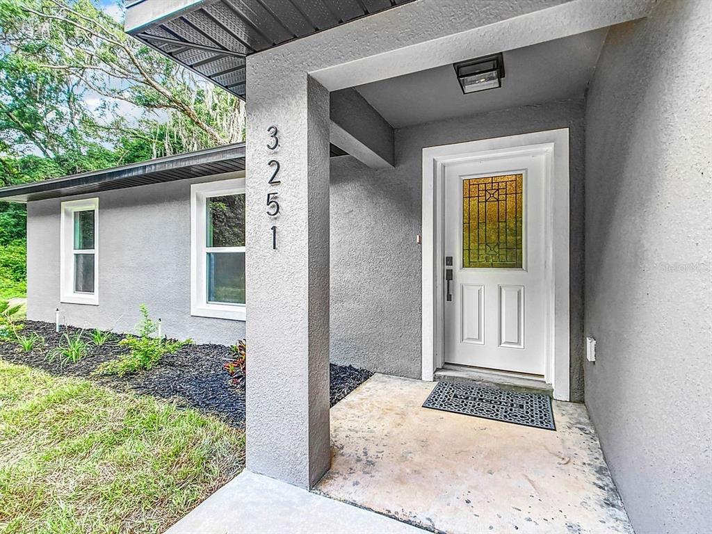 The exterior view shows a gray stucco house entrance with a white door and address numbers — 15500* NE 49 PLACE, WILLISTON, FL