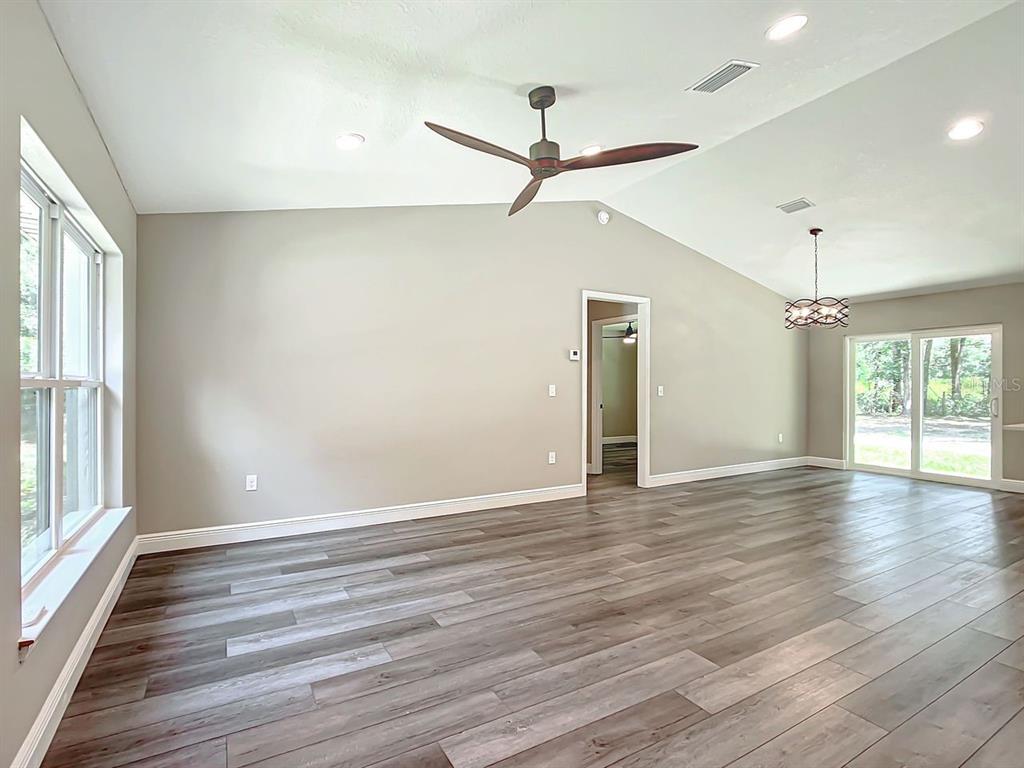 A spacious living room features vaulted ceilings, wood-look flooring, a ceiling fan, and sliding doors — 15500* NE 49 PLACE, WILLISTON, FL