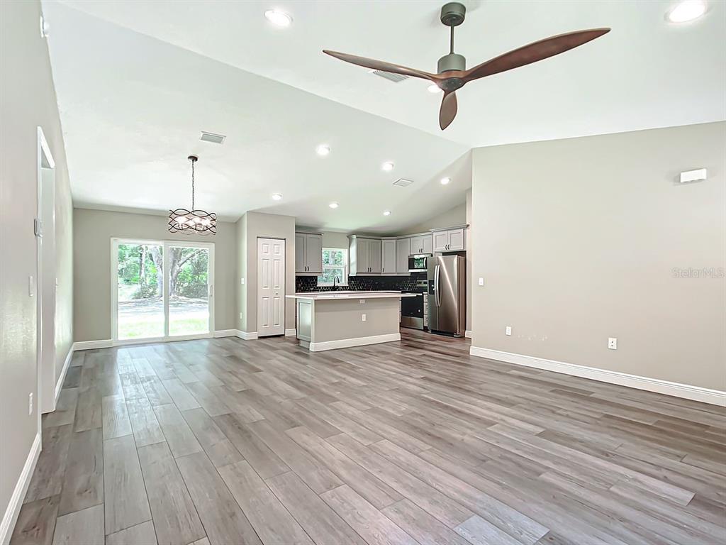 An open-concept kitchen and living area features wood-look flooring, a center island, and vaulted ceilings — 15500* NE 49 PLACE, WILLISTON, FL