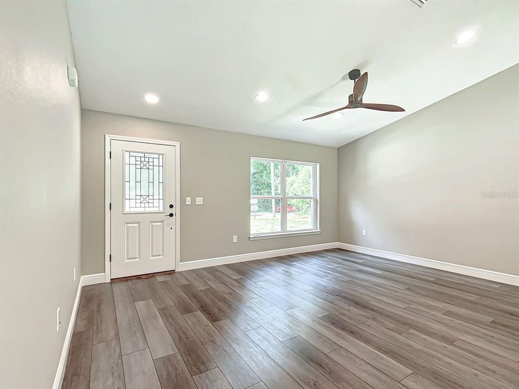 A room with light gray walls, wood-look flooring, a ceiling fan, and a front door — 15500* NE 49 PLACE, WILLISTON, FL