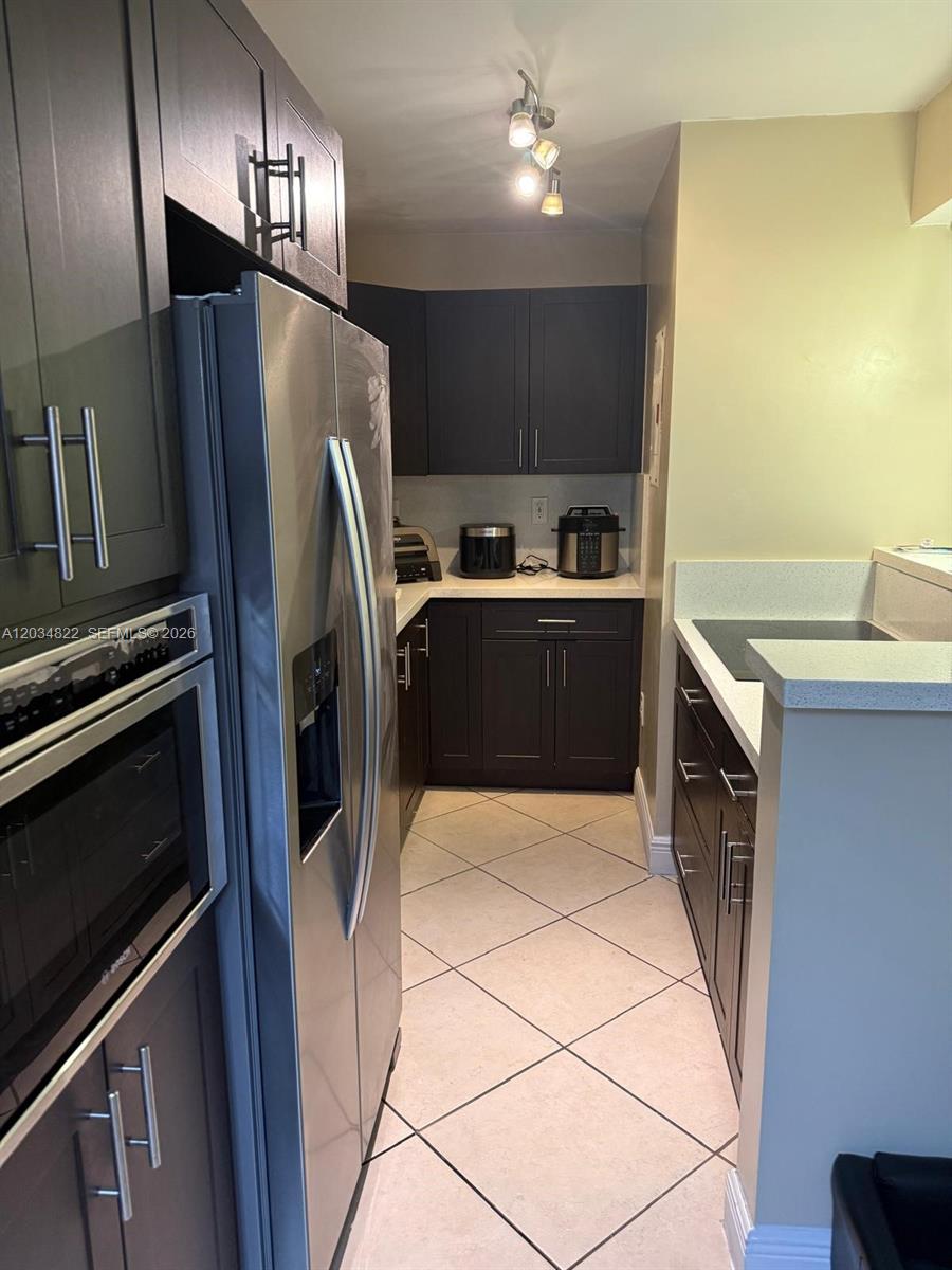 A galley kitchen features dark cabinetry, stainless steel appliances, and light-colored tile flooring — 7405 SW 152nd Ave # 107, Miami FL 33193, MIAMI, FL