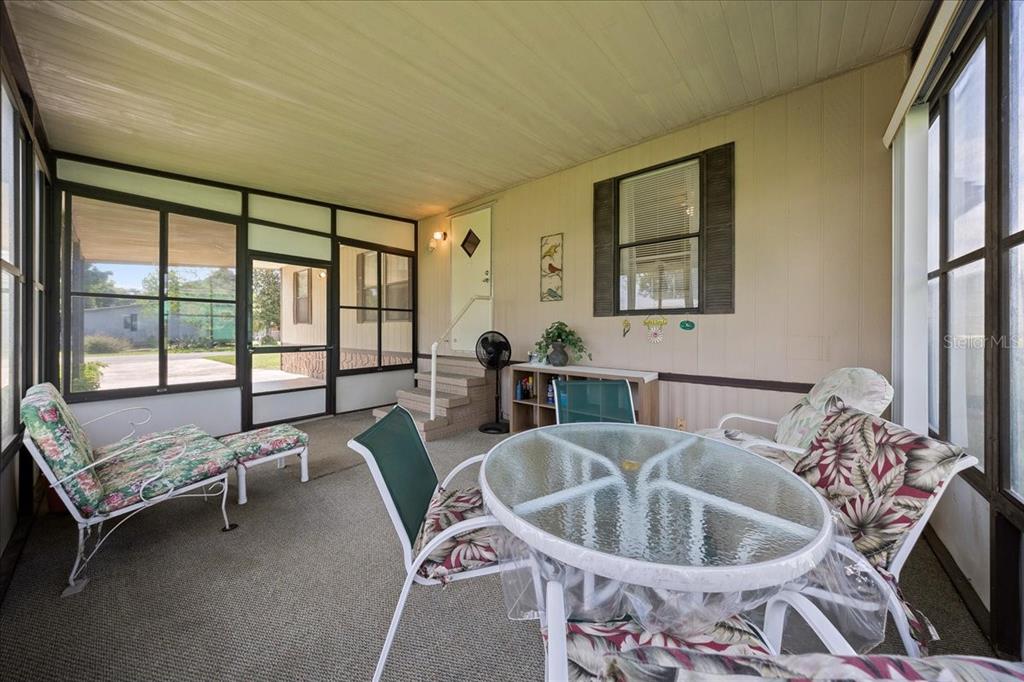 A screened-in porch features a glass-topped table, floral-patterned chairs, and a carpeted floor — 14716 SE 90TH TERRACE, SUMMERFIELD, FL