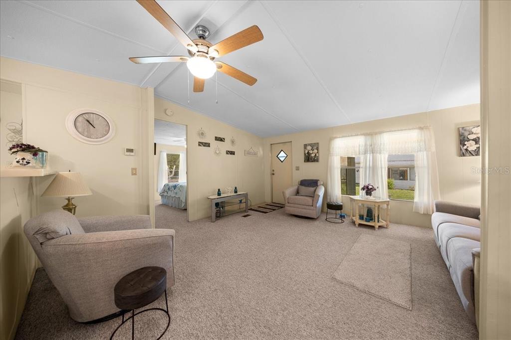 A living room with beige carpet, a ceiling fan, and a view into a bedroom — 14716 SE 90TH TERRACE, SUMMERFIELD, FL
