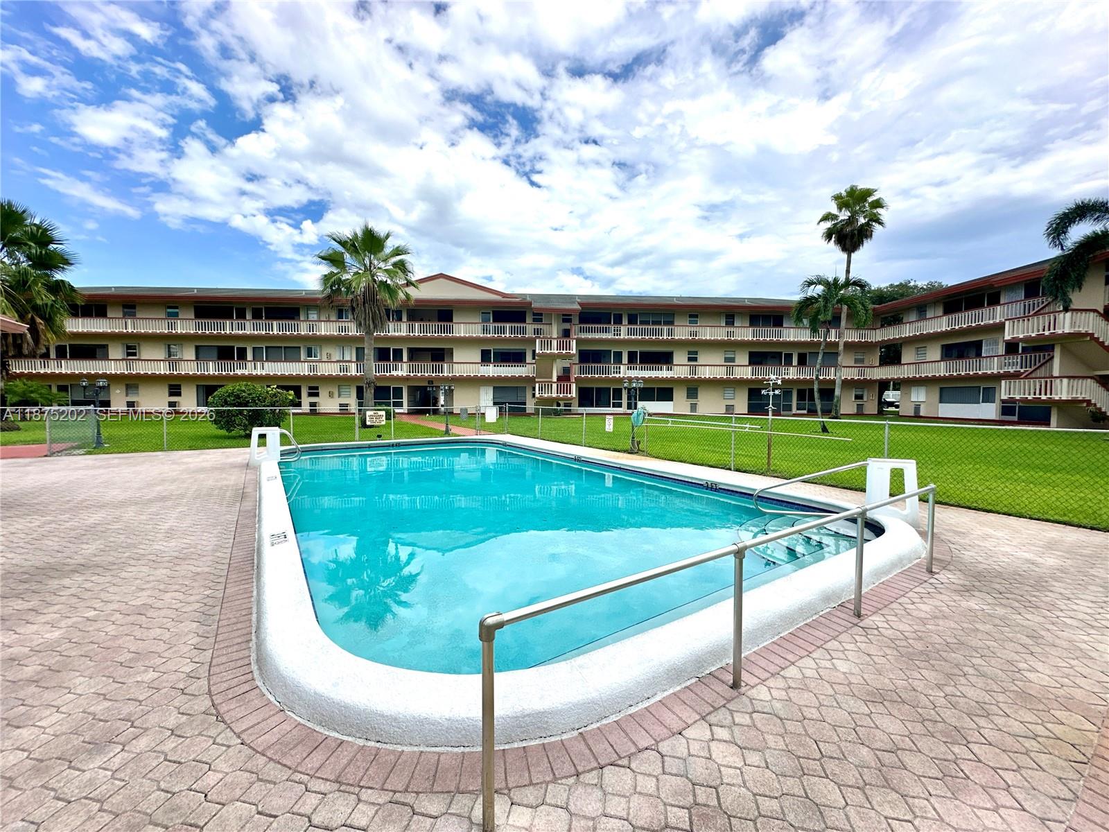 A rectangular swimming pool sits in front of a multi-story apartment building with balconies — 5300 Washington St # A139, Hollywood FL 33021, HOLLYWOOD, FL